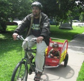 Photo of a man on a bike with a child in a bike trailer.